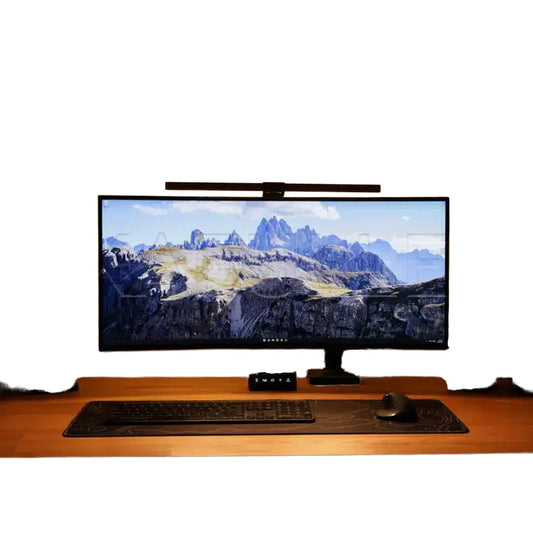 Wooden desk with a large monitor displaying a mountain landscape, keyboard, and mouse on a white background.