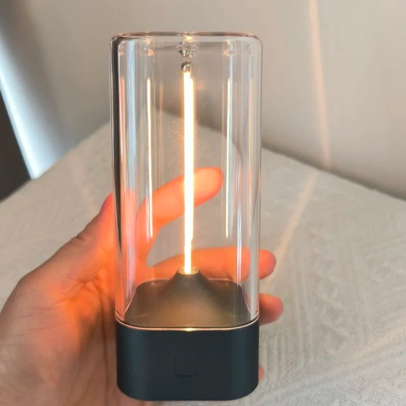 Hand holding a clear cylindrical light with a black base on a white surface.