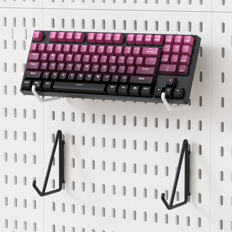Mechanical keyboard with pink and black keys mounted on a pegboard wall.