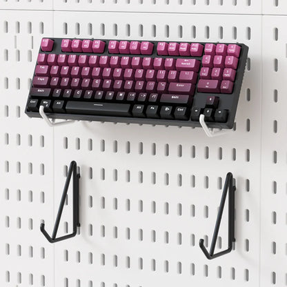 Mechanical keyboard with pink and black keys mounted on a pegboard wall.