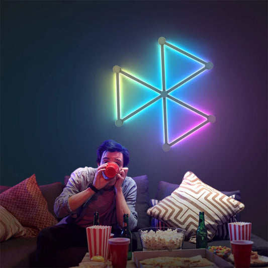 Person sitting on a couch with popcorn and drinks, colorful geometric light fixture on the wall.