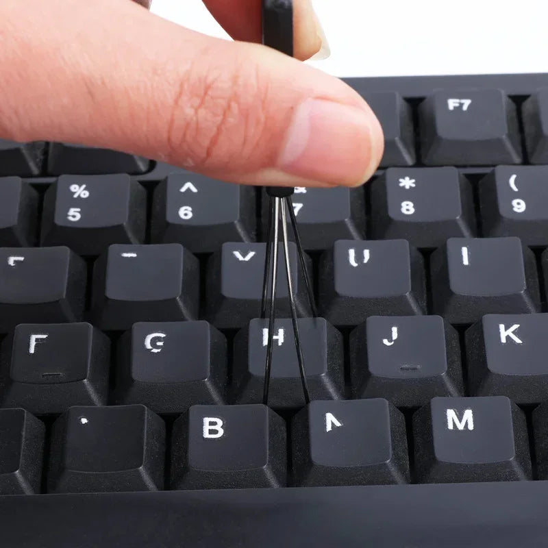 Close-up of a person using a tool to remove a key from a black keyboard.