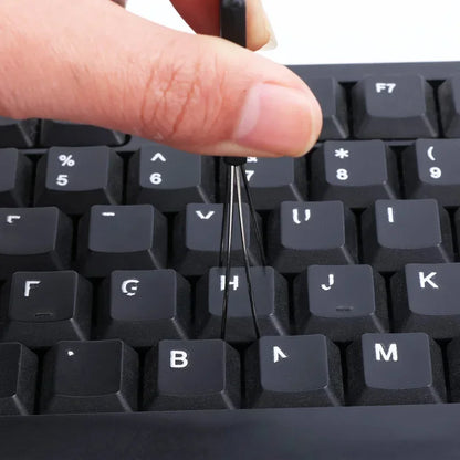 Close-up of a person using a tool to remove a key from a black keyboard.