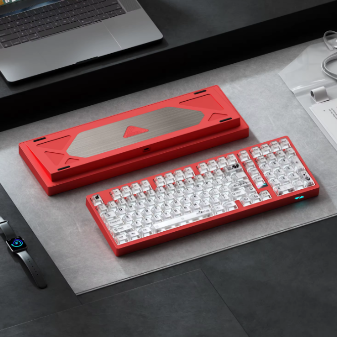 Red mechanical keyboard on a desk with a laptop and smartwatch in the background